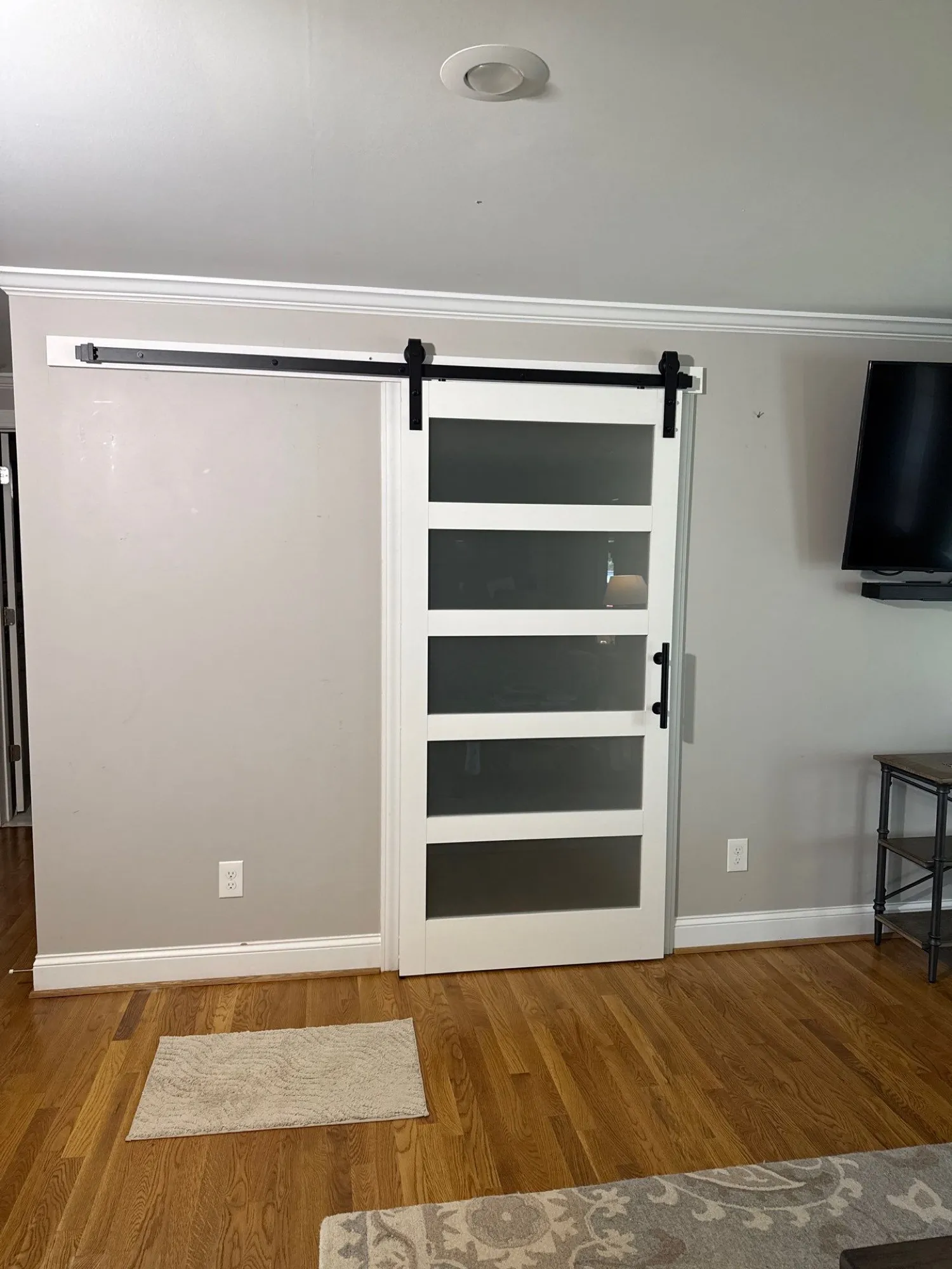 White sliding barn door hung on a black wall-mounted track and rollers