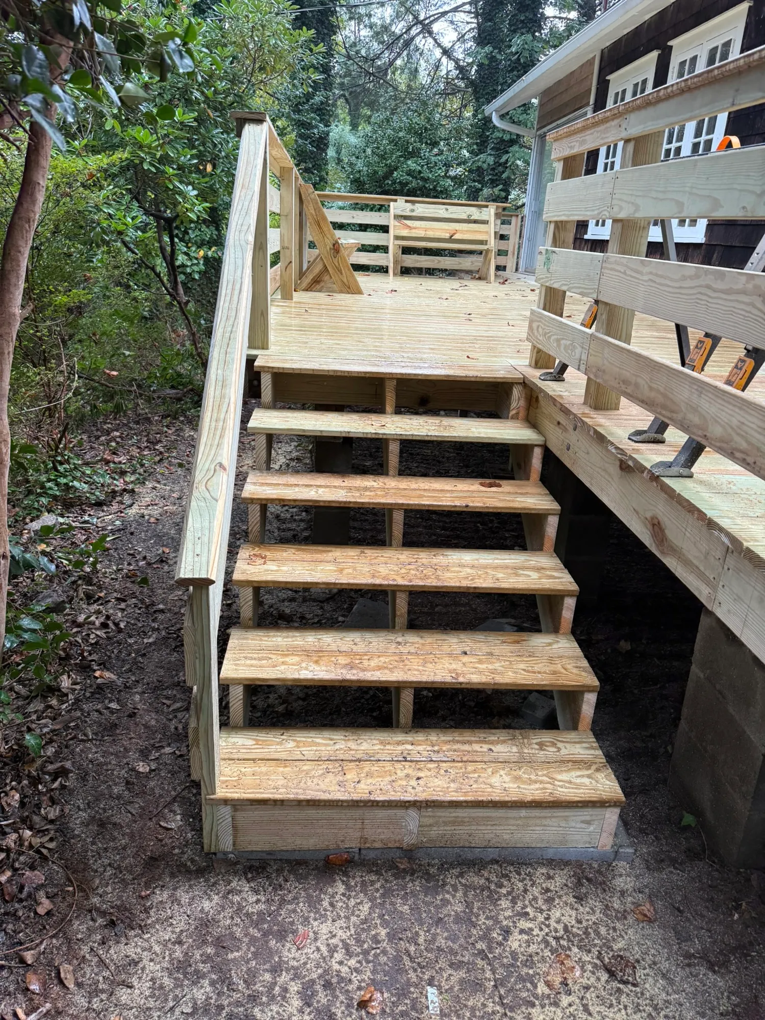 New pressure-treated deck stairs with open risers and a handrail leading up to a deck