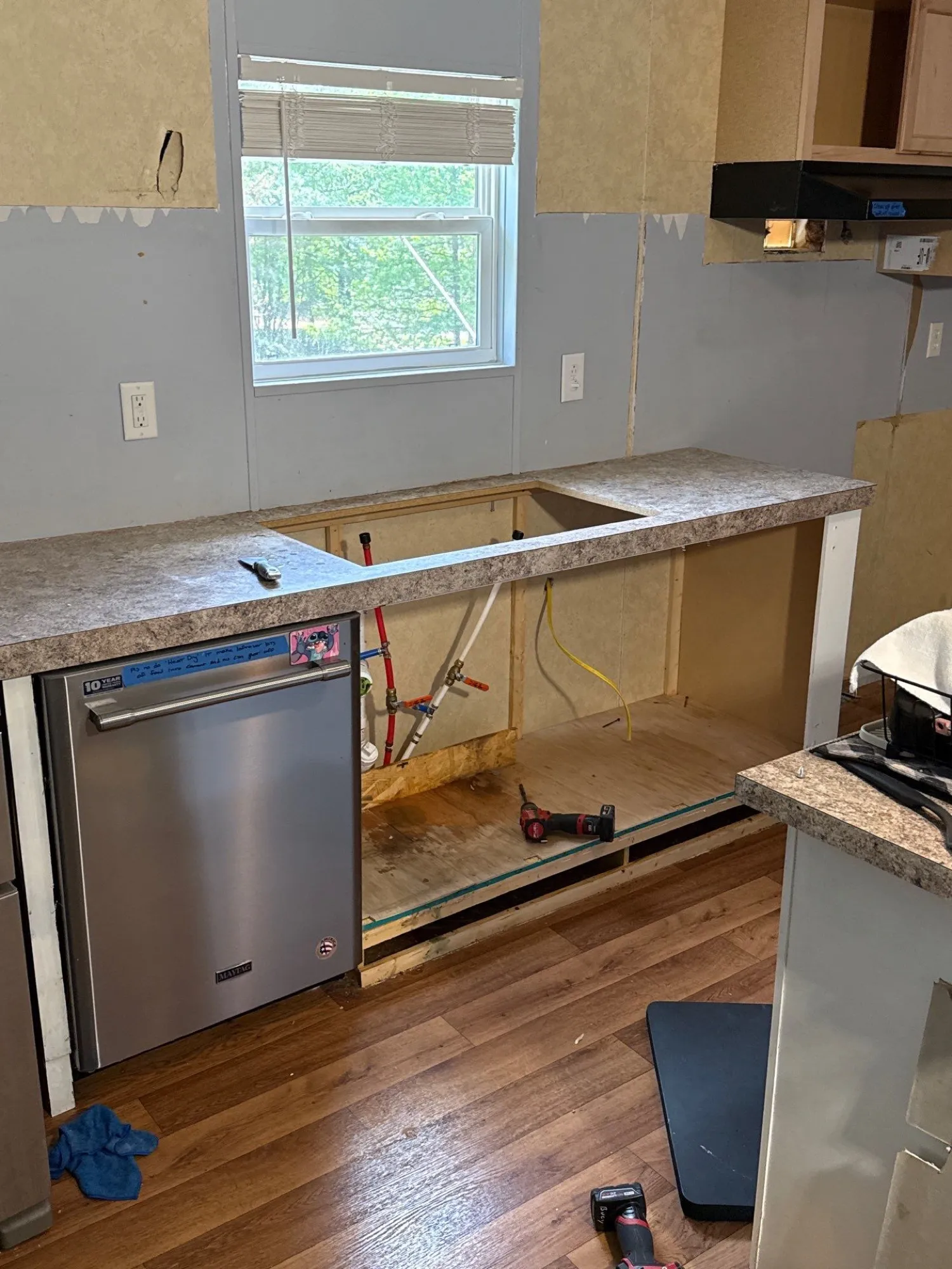 Sink base cabinet opened up during a repair, showing PEX supply lines and shutoff valves beside a dishwasher